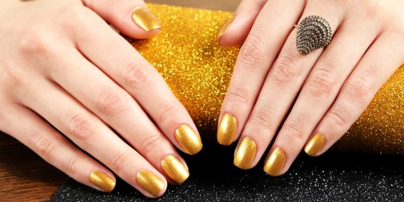 Woman showing manicured hands with golden nail polish on table, closeup